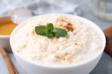 Tasty rice pudding with cinnamon, mint and honey on light grey table, closeup