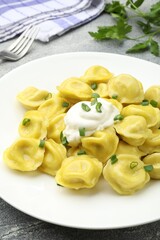 Tasty dumplings with green onion and sour cream on grey textured table, closeup