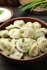 Tasty dumplings with green onion and dill in bowl on wooden table, closeup