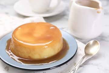 Delicious pudding with caramel sauce and spoon on white marble table, closeup