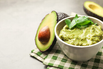 Tasty avocado dip in bowl, parsley and fruits on grey table, closeup. Space for text