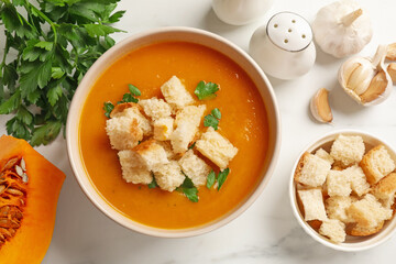 Tasty pumpkin cream soup with croutons and parsley in bowl on white table, flat lay
