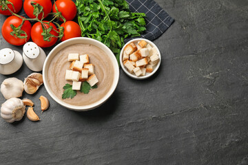Delicious mushroom cream soup with croutons, parsley and ingredients on black textured table, flat lay. Space for text