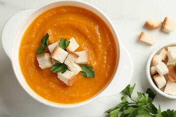 Tasty pumpkin cream soup with croutons and parsley in bowl on white table, flat lay