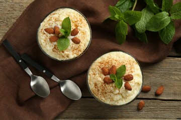 Delicious rice pudding with cinnamon, almonds and mint served on wooden table, flat lay