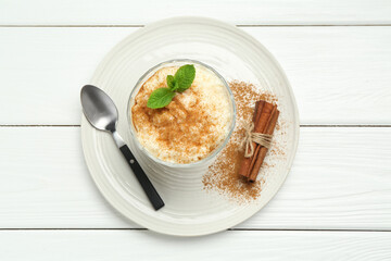 Delicious rice pudding with cinnamon, mint and spoon on white wooden table, top view