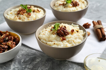 Delicious rice pudding with walnuts, cinnamon, mint and honey on grey table, closeup