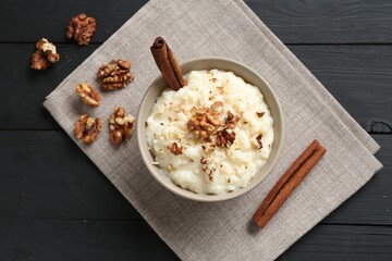 Delicious rice pudding with walnuts and cinnamon on black wooden table, flat lay