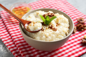Delicious rice pudding in bowl, walnuts, mint, honey and spoon on table, closeup