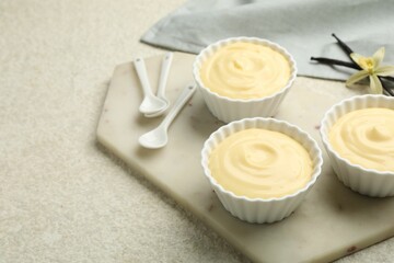 Tasty vanilla pudding with spoons, pods and flower on light textured table. Space for text