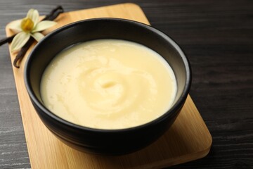 Tasty vanilla pudding in bowl, flower and pods on wooden table, closeup
