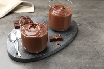 Tasty pudding and pieces of chocolate on grey table