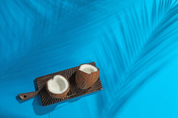 Fresh coconut and shadow cast by tropical palm on light blue background, top view. Space for text