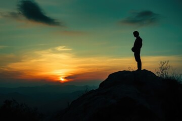 Silhouette of a person standing on a mountain top, watching a vibrant sunset over the horizon.