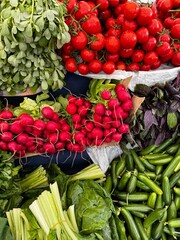 A vibrant display of fresh vegetables at a farmers market, featuring ripe red tomatoes, radishes, cucumbers, celery, and leafy greens. Perfect for themes of healthy eating, organic produce.
