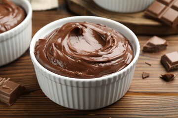 Tasty pudding in bowls and pieces of chocolate on wooden table, closeup