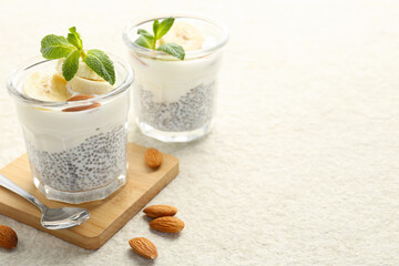 Delicious dessert with chia seeds, yogurt, banana, almond and mint in glasses on light textured table, closeup with space for text. Superfood
