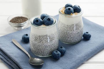 Delicious pudding with chia seeds, yogurt, blueberries and granola in glasses on white wooden...