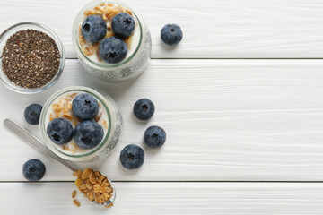 Delicious pudding with chia seeds, yogurt, blueberries and granola on white wooden table, flat lay with space for text. Superfood