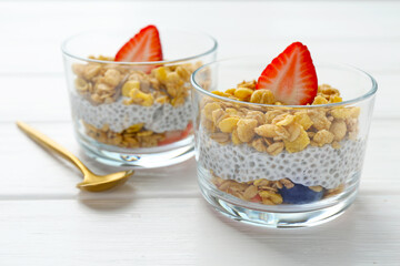 Delicious dessert with chia seeds, yogurt, granola and strawberries in glasses on white wooden table, closeup. Superfood