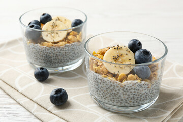 Delicious dessert with chia seeds, yogurt, granola, blueberries and banana on white wooden table, closeup. Superfood