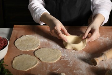 Making khinkali. Woman shaping piece of dough at table in kitchen, closeup