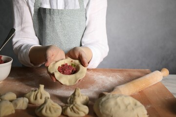 Woman making khinkali on table in kitchen, closeup