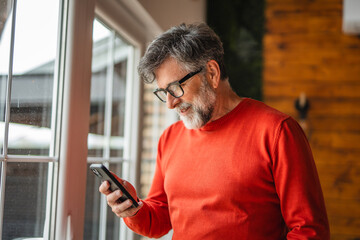 Relax senior man stand by the window and use mobile phone