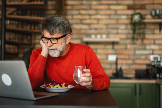 senior mature man enjoy at home while eat salad and use laptop