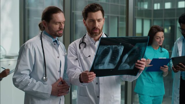 Two Caucasian males men doctors interns talking about patient result x-ray image lungs surgeon and therapist radiologist consulting discussion diagnosis fluoroscopy speaking indoors hospital hallway