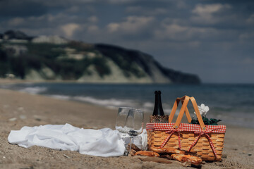 Elegant beach picnic with wine glasses and food by the sea under cloudy sky