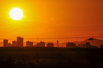 A commercial airplane approaches Sky Harbor International Airport as the sun sets behind the Phoenix skyline, viewed from Tempe Town Lake, illustrating the intense heat of Arizona's Valley of the Sun