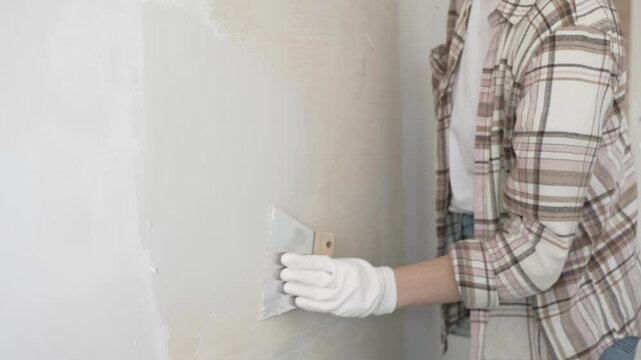 Unknown female construction worker wearing protective gloves applying plaster, smoothing wall surface during home renovation work