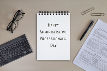 Flat lay of spiral notebook with Happy Administrative Professionals Day message on office desk with...