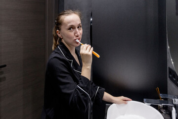 A woman in comfy pajamas brushes her teeth in a modern bathroom, enjoying her daily selfcare...