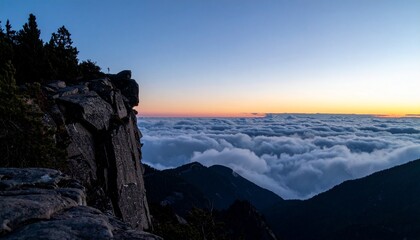Obraz premium Wide shot from the edge of a mountain cliff at twilight with low clouds rolling in below
