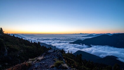 Obraz premium Wide shot from the edge of a mountain cliff at twilight with low clouds rolling in below