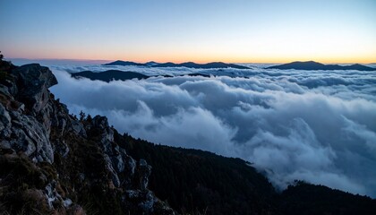 Naklejka premium Wide shot from the edge of a mountain cliff at twilight with low clouds rolling in below