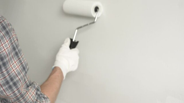 Close up focusing on gloved hand rolling white paint across wall surface, applying smooth, even coating during residential interior painting renovation