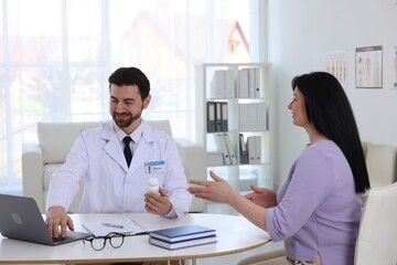 Doctor with bottle of pills consulting patient at table in hospital
