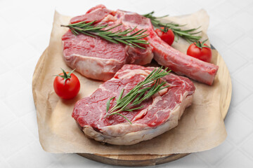 Pieces of raw beef, rosemary and tomatoes on white tiled table, closeup