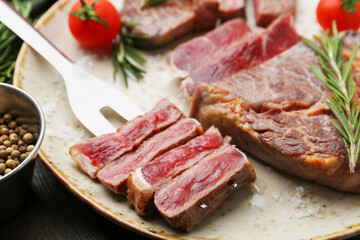 Pieces of delicious beef meat, spices and tomatoes on table, closeup