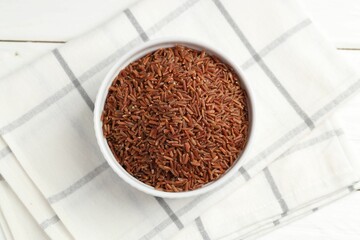 Raw brown rice in bowl on white wooden table, top view