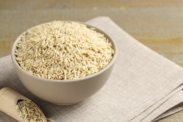 Raw brown rice in bowl and scoop on table, closeup