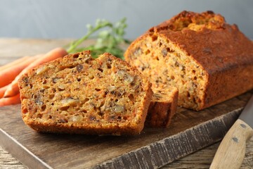 Homemade carrot cake with nuts, knife and vegetables on wooden table, closeup