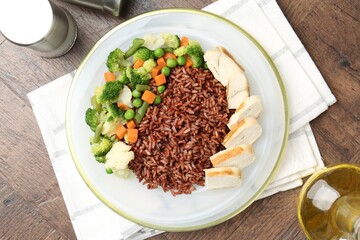 Delicious brown rice with chicken and vegetables served on wooden table, flat lay