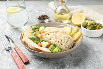 Delicious brown rice with chicken, vegetables and lemon slices served on grey textured table, closeup
