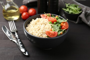 Delicious brown rice with vegetables on black wooden table, closeup