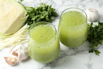 Healthy parsley smoothie in glasses, garlic, cabbage and leaves on white marble table, closeup