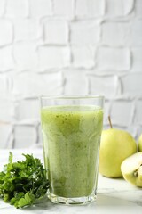 Healthy parsley smoothie in glass, leaves and apples on white marble table against grey textured background, closeup